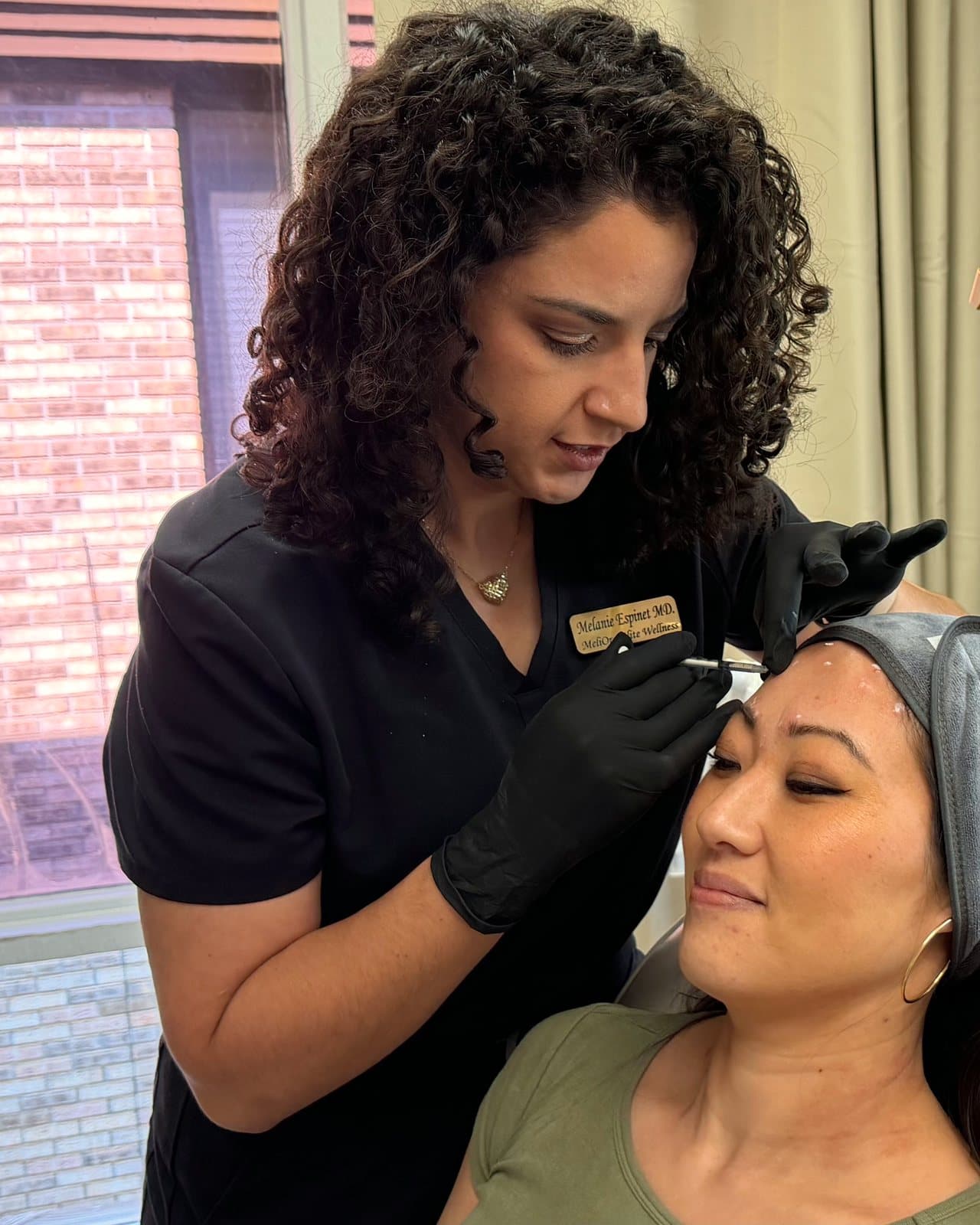 Dr. Espinet in black scrubs injecting the forehead of a patient wearing a gray headband and an olive T-shirt