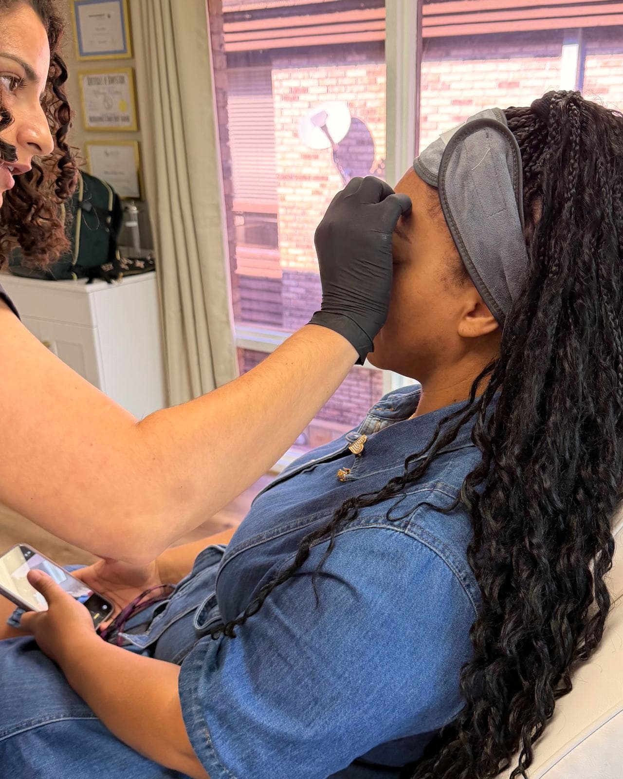 Dr. Espinet treating the forehead of a reclined patient in a denim dress who holds her phone