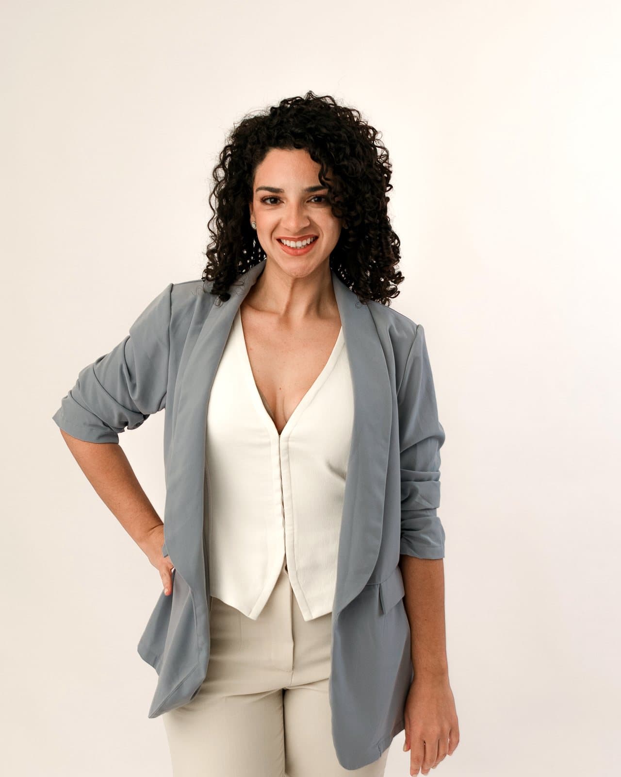 Dr. Melanie Espinet smiling in a gray blazer over a white vest, one hand on her hip