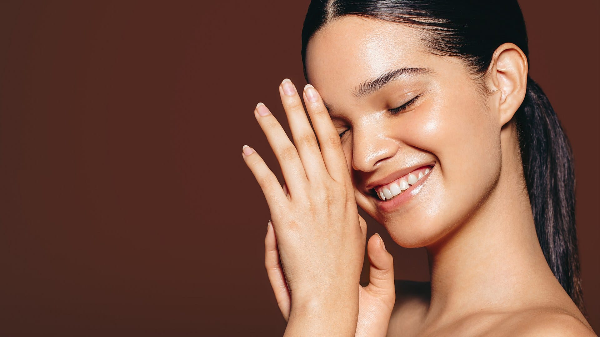 A woman with glowing skin gently resting her hands against her face